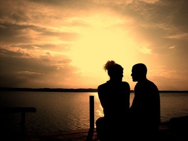 Siluetas de dos personas sentadas junto al agua al atardecer