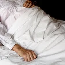 Persona recostada en una cama con sábanas blancas